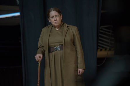 Ann Dowd wearing khaki outfit and holding a cane with a serious expression