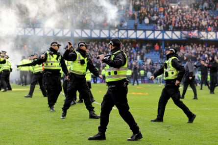 Police officer and stewards form a line to separate the fans on the pitch after the end of the game.