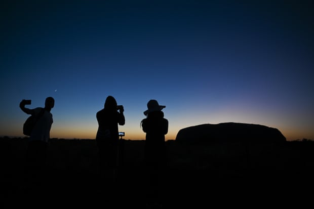 Tourists take pictures of Uluru just before sunrise.