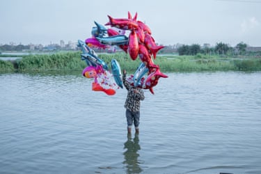 A person stands in a river holding ballons in the shape of fish