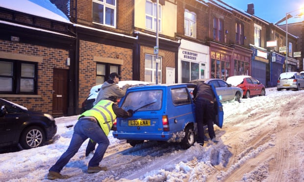 People in Sheffield struggle to push their car  through the snow