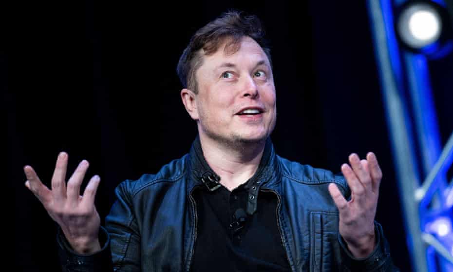 Elon Musk smirks, both hands up in an uncertain gesture.