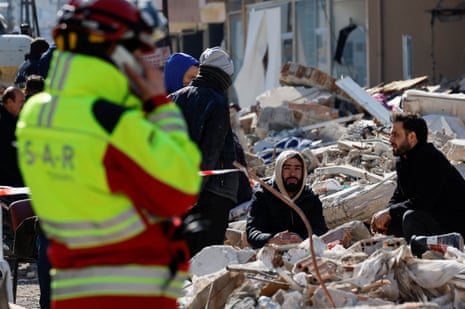 Des hommes sont assis au milieu de l'épave alors que des membres de l'équipe allemande de recherche et de sauvetage internationale (ISAR) travaillent sur le site d'un bâtiment effondré à Kirikhan.