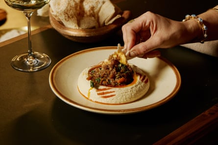 A hand dipping bread into a plate of hummus with king prawns and spanner crab.