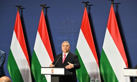 Viktor Orbán speaks at a lectern with Hungarian flags in the background.