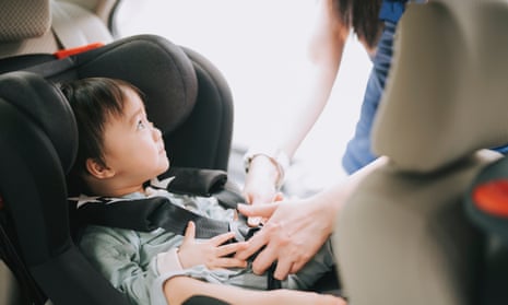 Mother buckling up baby boy in car seat.