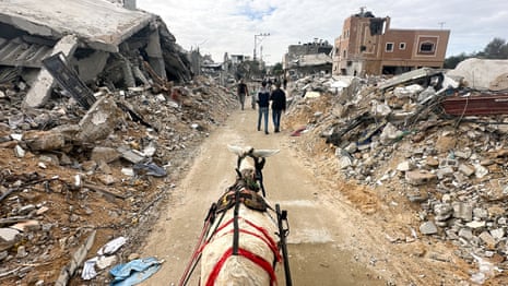 A donkey drawing a cart moves past the ruins of Palestinian houses destroyed in Israeli strikes.