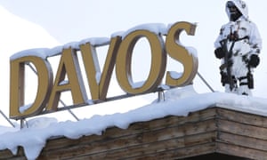 An
        armed officer is snow camouflage stands guard on a snow-covered
        roof by the big Davos sign