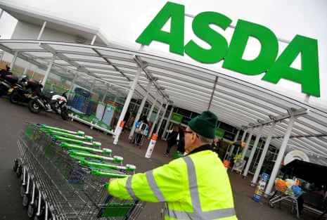 A worker pushes shopping trolleys at an Asda store in West London.