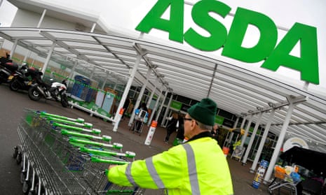 A worker pushes shopping trolleys at an Asda store in West London.