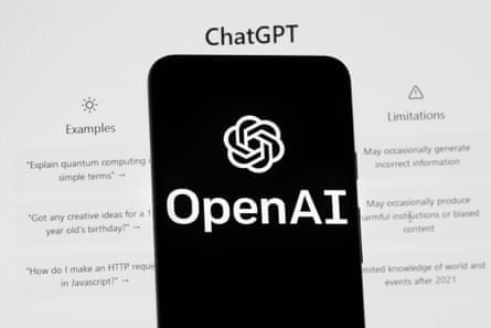 The OpenAI logo is seen on a mobile phone in front of a computer screen displaying the ChatGPT home screen.