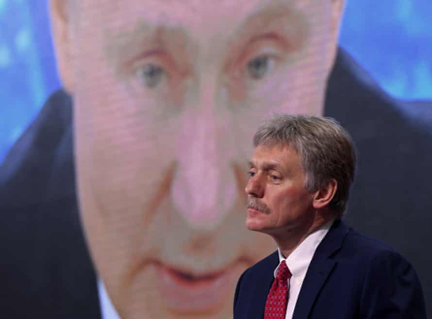 Kremlin spokesman Dmitry Peskov sits in front of a screen displaying Russian President Vladimir Putin.