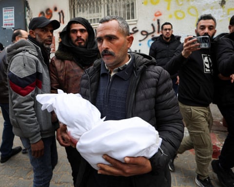 A man carries a small body in white funeral shrouds