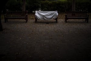 A homeless man covered by a sheet sleeps on a bench at a public park in Barcelona, Spain