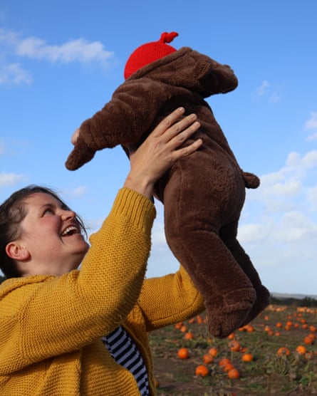 Nicola wearing a yellow jumper holding her baby in the air with a field of pumpkins in the background.