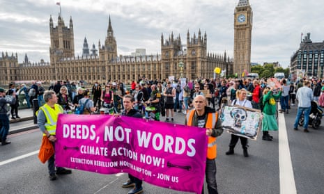 Just Stop Oil and Extinction Rebellion activists on Westminster bridge, holding up placards and posters and a banner reading 'deeds, not words - climate action now'