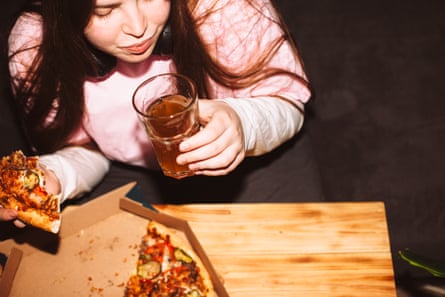 Young woman eating pizza and drinking craft beer at house party