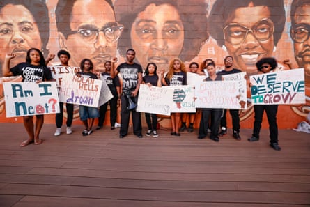 Young people hold signs in front of a mural of people's faces