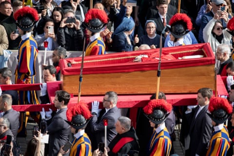 Open casket surrounded by Swiss Guards is taken through the crowd in the square.