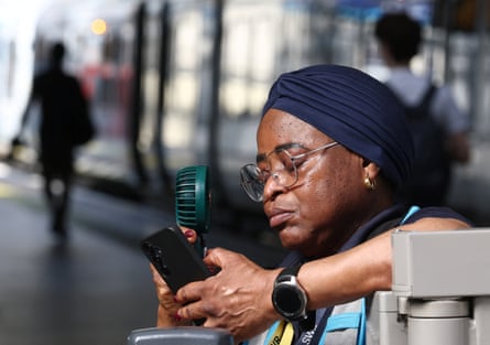A revenue protection officer uses a fan to cool down on a railway platform