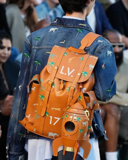 A model wears a denim jacket while carrying a tan leather rucksack with matching palm tree and animal motifs