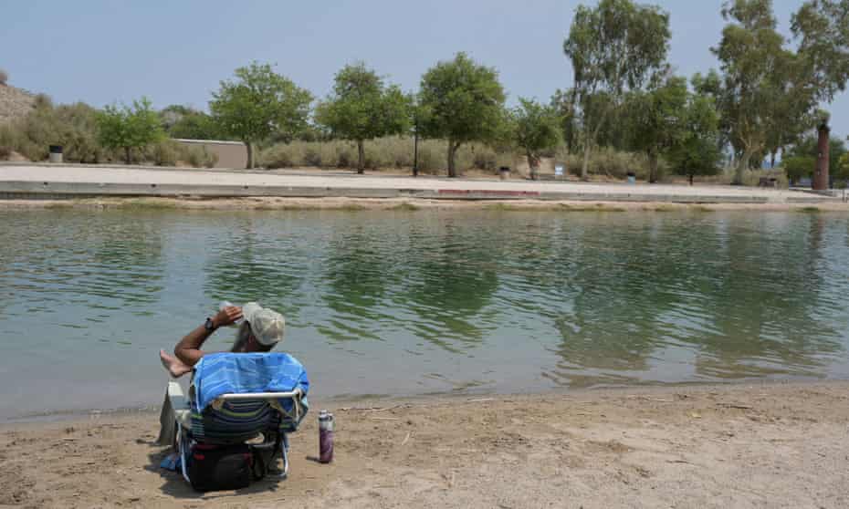A man drinks from a bottle of water while sitting on an aluminum beach chair on the shore of Lake Havasu.