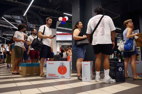 People queue to buy pedestal fans and humidifiers at an electronics and homeware store. Their purchases can be seen in illustrated boxes beside them as they stand in line.