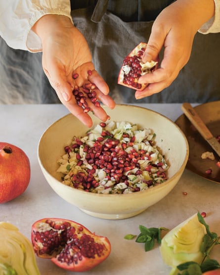 A pair of hands tumbling pomegranates seeds into a bowl of diced fennel. 