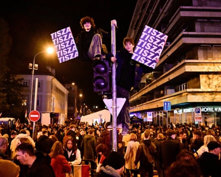 Boys perched on a traffic light hold Tisza signs amid celebrations in Budapest.