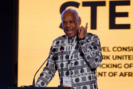 Hilary Beckles gives a speech. He is in his early 70s and wears a black and white patterned shirt. He looks animated.