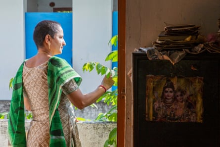 A woman with cropped hair stands in a sunny doorway looking out