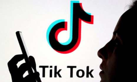 A person holds a smartphone as TikTok logo is displayed behind them.