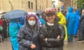 Ekaterine Burkadze with her nephew Paata Kaloiani both wearing black rain jackets with goggles on their heads and she has a facemask. People in colourful rain jackets behind them
