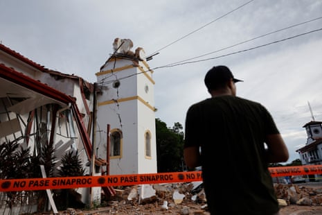 A man watches the earthquake-damaged San Juan Bautista Cathedral behind orange hazard tape