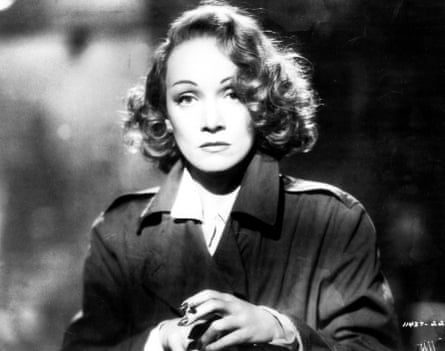 A black and white photo of Marlene Dietrich in a raincoat, holding a cigarette
