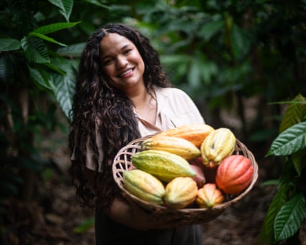 a woman smiles while holding a basket of cocoa plants