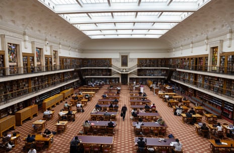 A grand room with people at tables and walls covered by books