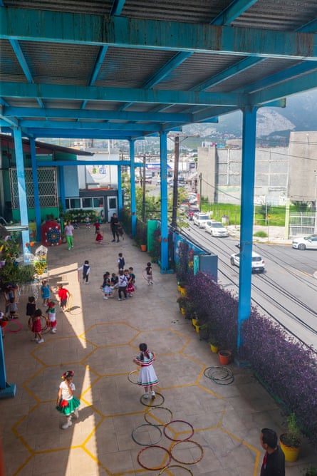 Children play in a courtyard with a large industrial facility in the background.