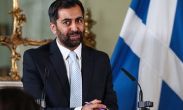 Humza Yousaf stands in front of a Scottish flag during a press conference