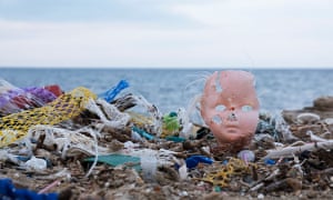 Plastic waste, including a doll's head, on the beach.