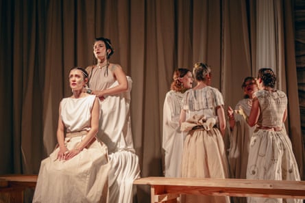 Seven women in white long dresses perform on stage in a play