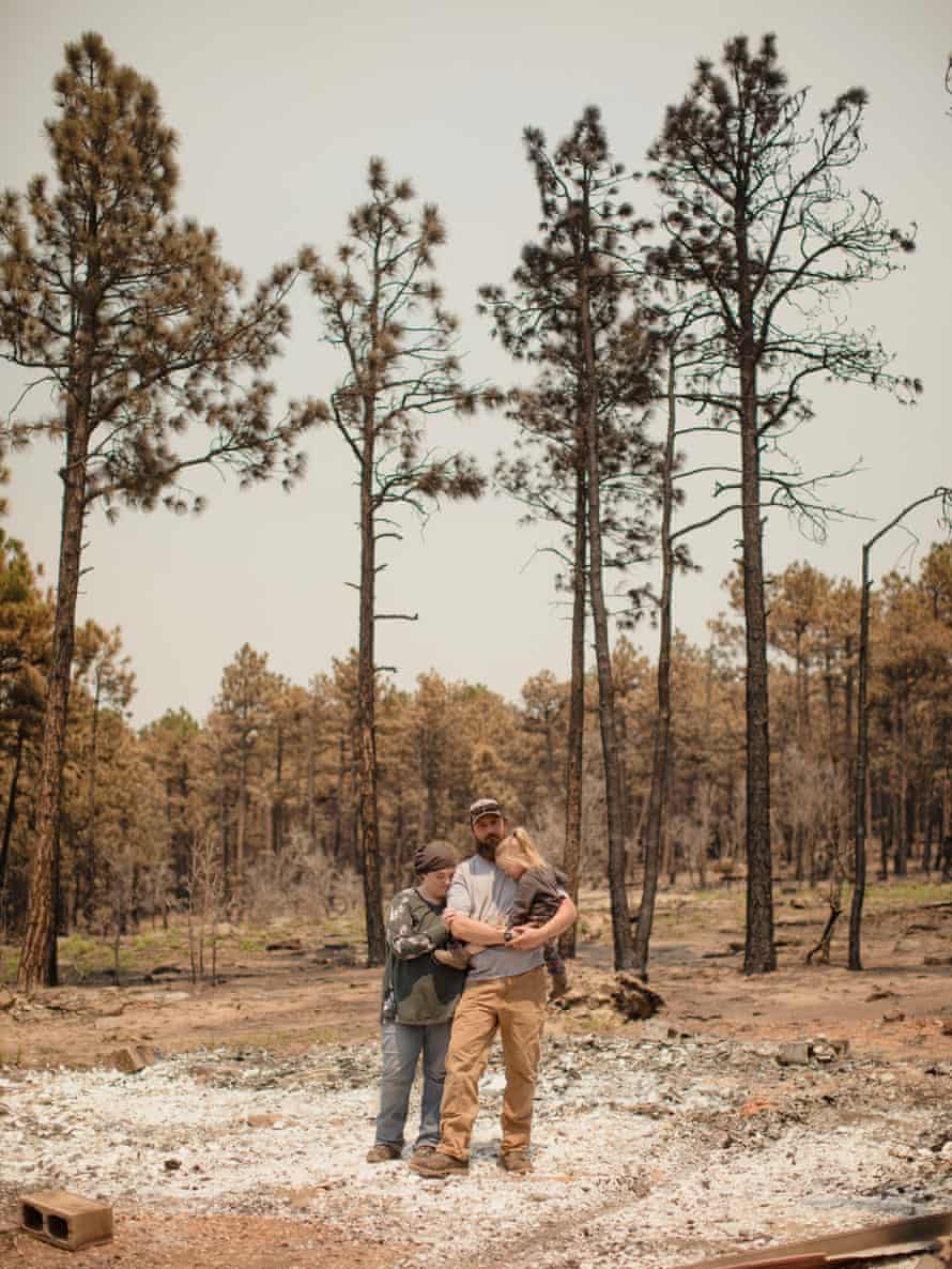 family hugs amid debris, in front of trees