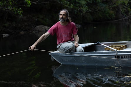 Bino, wearing a red T-shirt and grey pants, sits in  dinghy on the river