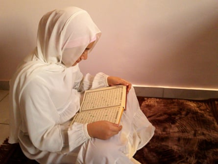 Girl in white veil and robes reads the Qur’an