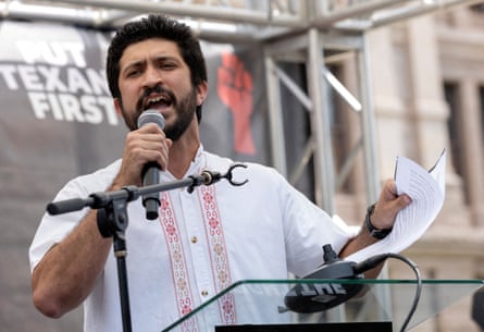 man in white shirt speaks into microphone outside