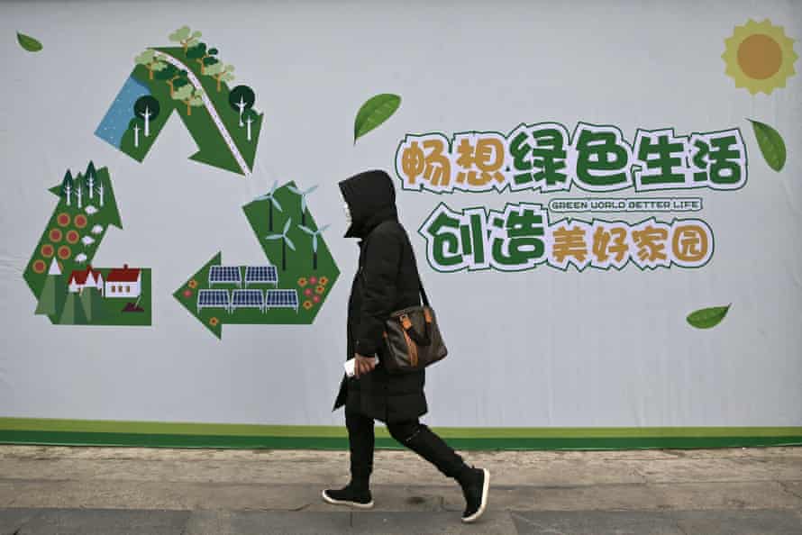 A woman in China walks past a recycling/environmental sigh