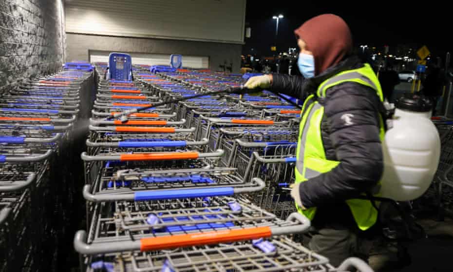 A worker sanitizes shopping carts as people line up in the early morning at Walmart on Black Friday.