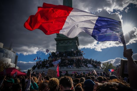 A large French flag waves over protesters gathered around a monument during a school protest