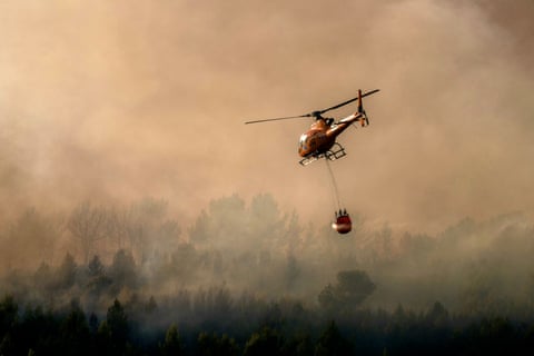 A firefighter water bomber helicopter flies over a wildfire raging in Pouzols-Minervois, southwestern France