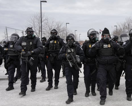Federal agents with black body armor, guns and gas masks.